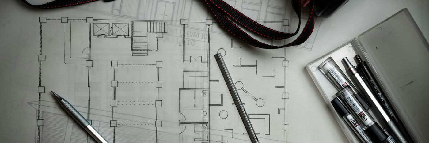 Architectural blueprints with drafting pencils, a metal ruler, and a storage tube